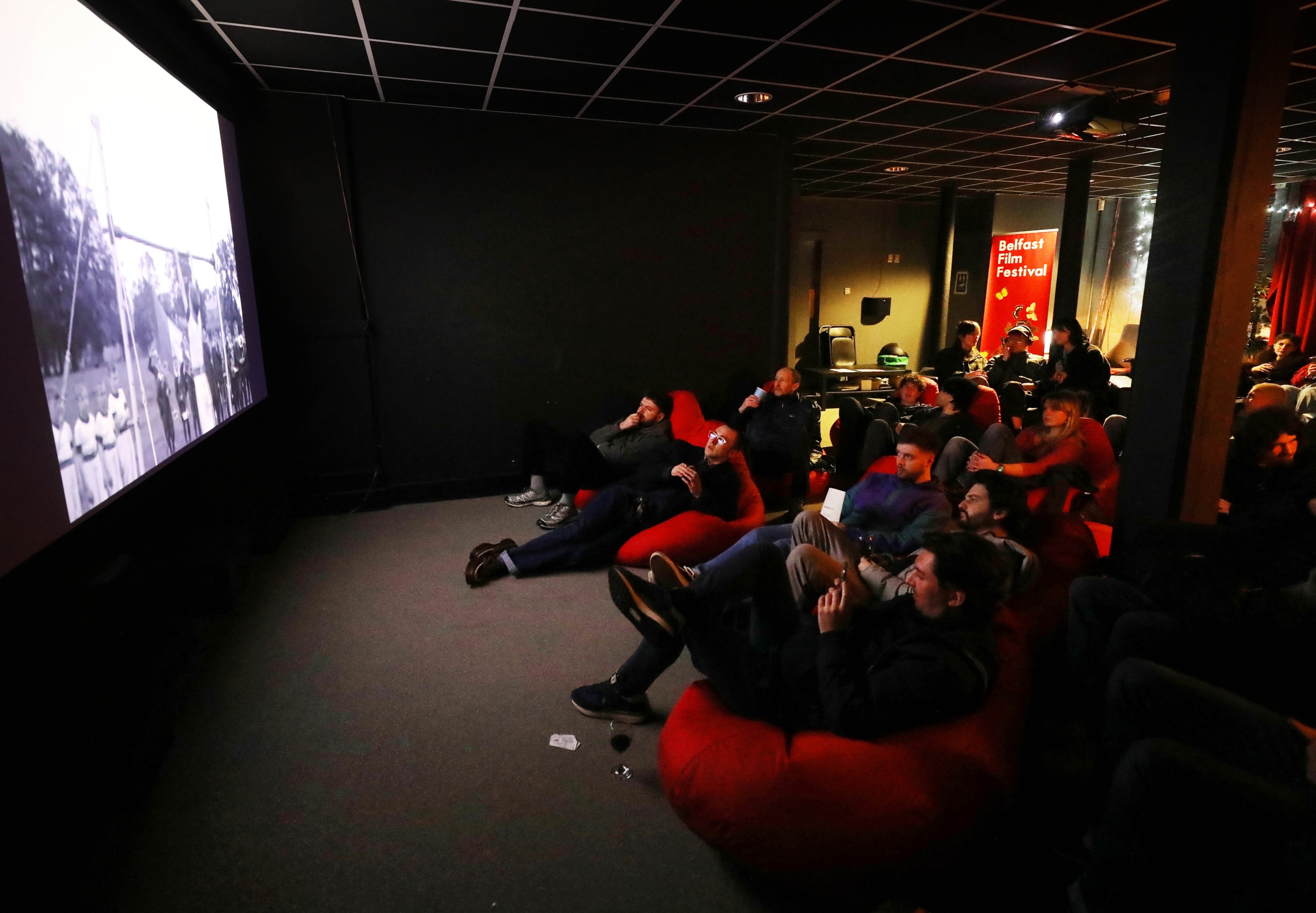 Audience members sit in bean bags and watch a film on screen at the left.
